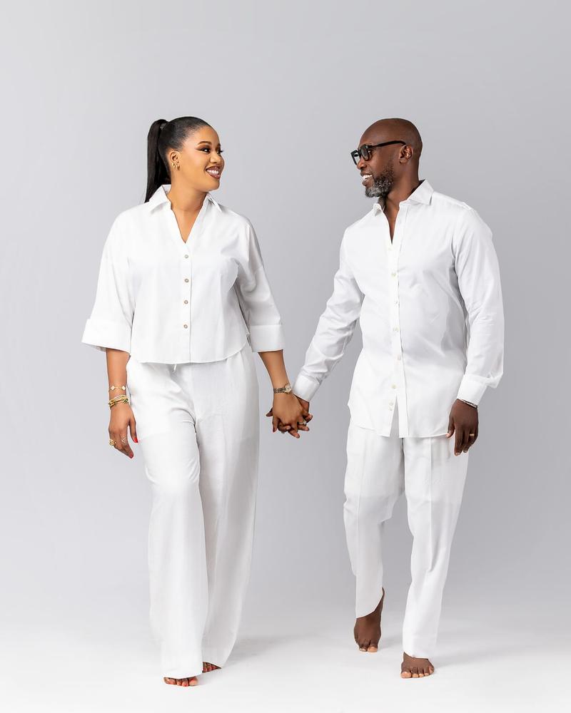 A couple in white linen walking hand in hand across the studio