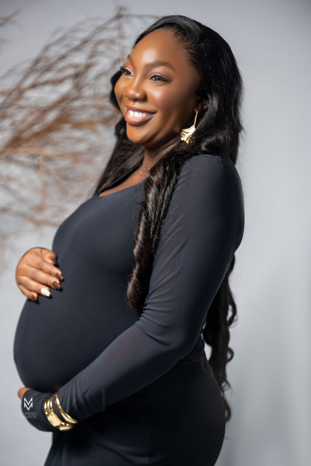 A pregnant woman in a fitted black dress smiling, hand on her bump