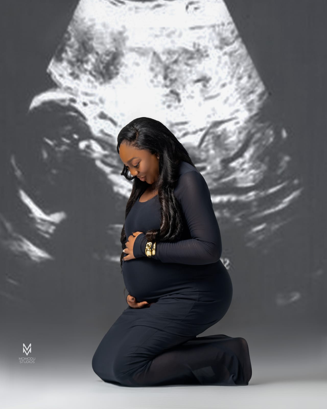 A pregnant woman kneeling in black in front of a projected ultrasound image