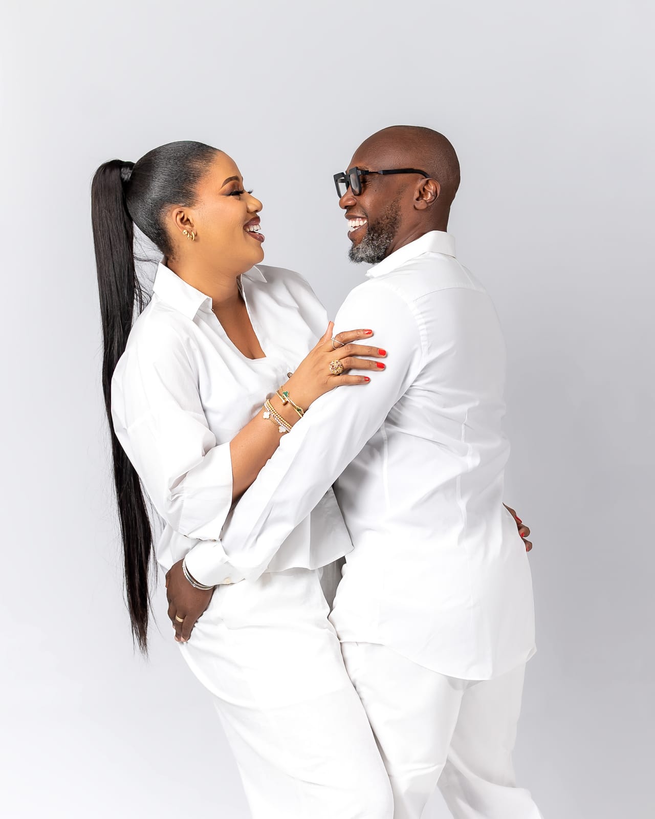 A couple in white laughing and embracing in the studio