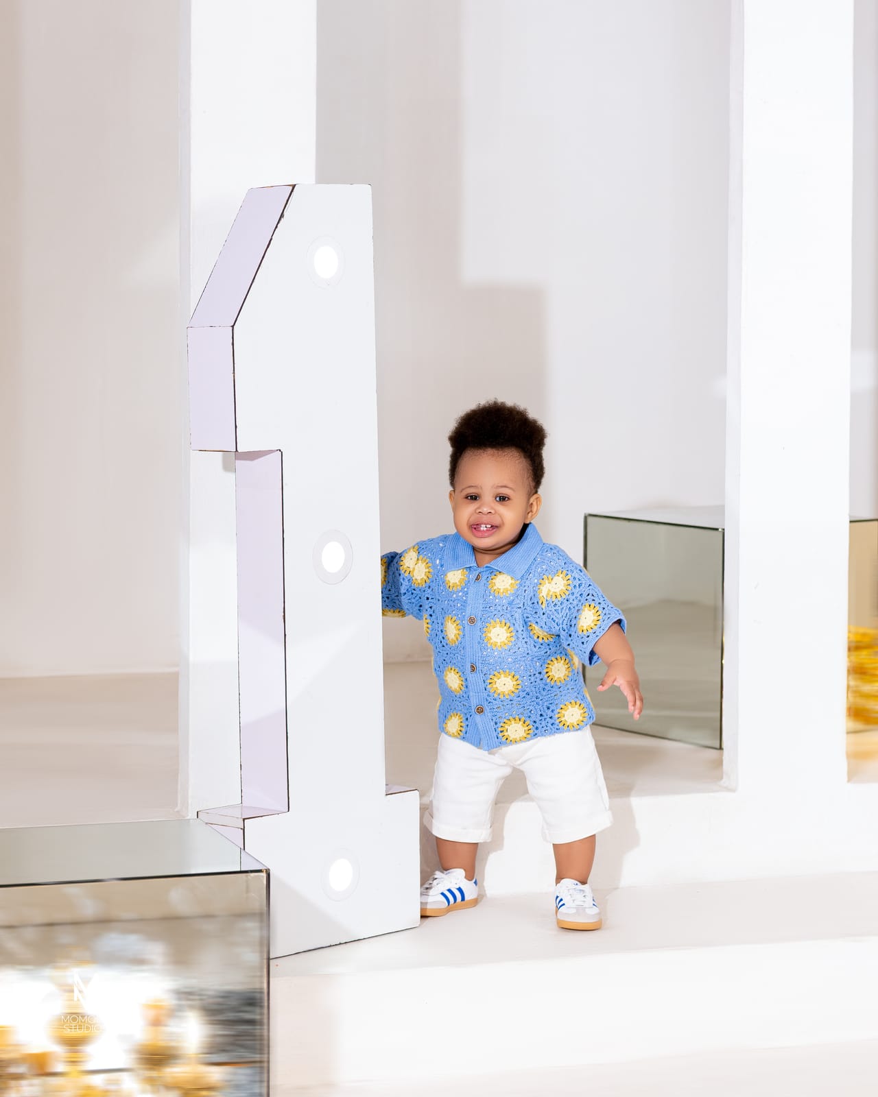 A toddler in a patterned shirt standing beside a large number one