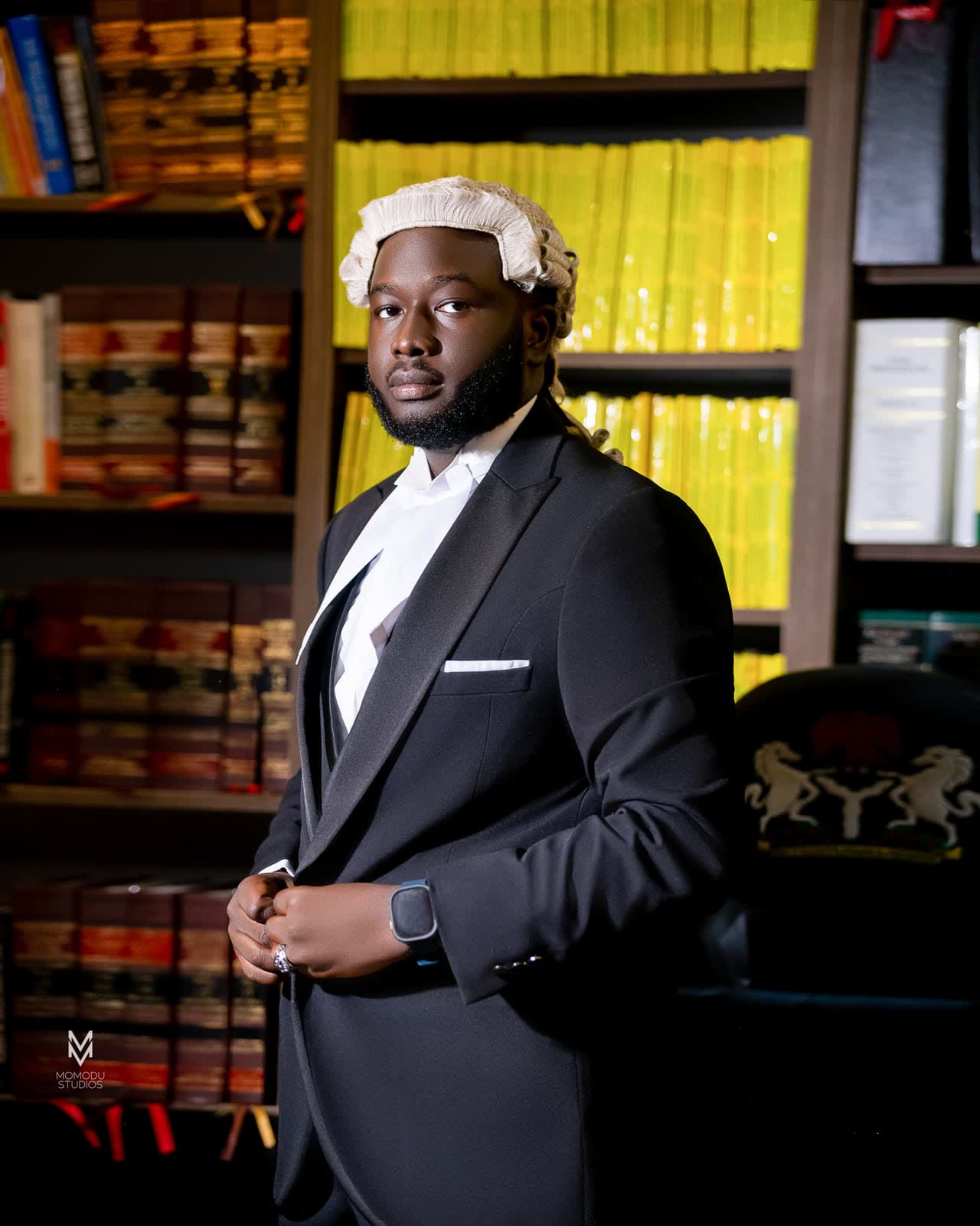 A new lawyer in a barrister's wig and suit standing before a wall of law books