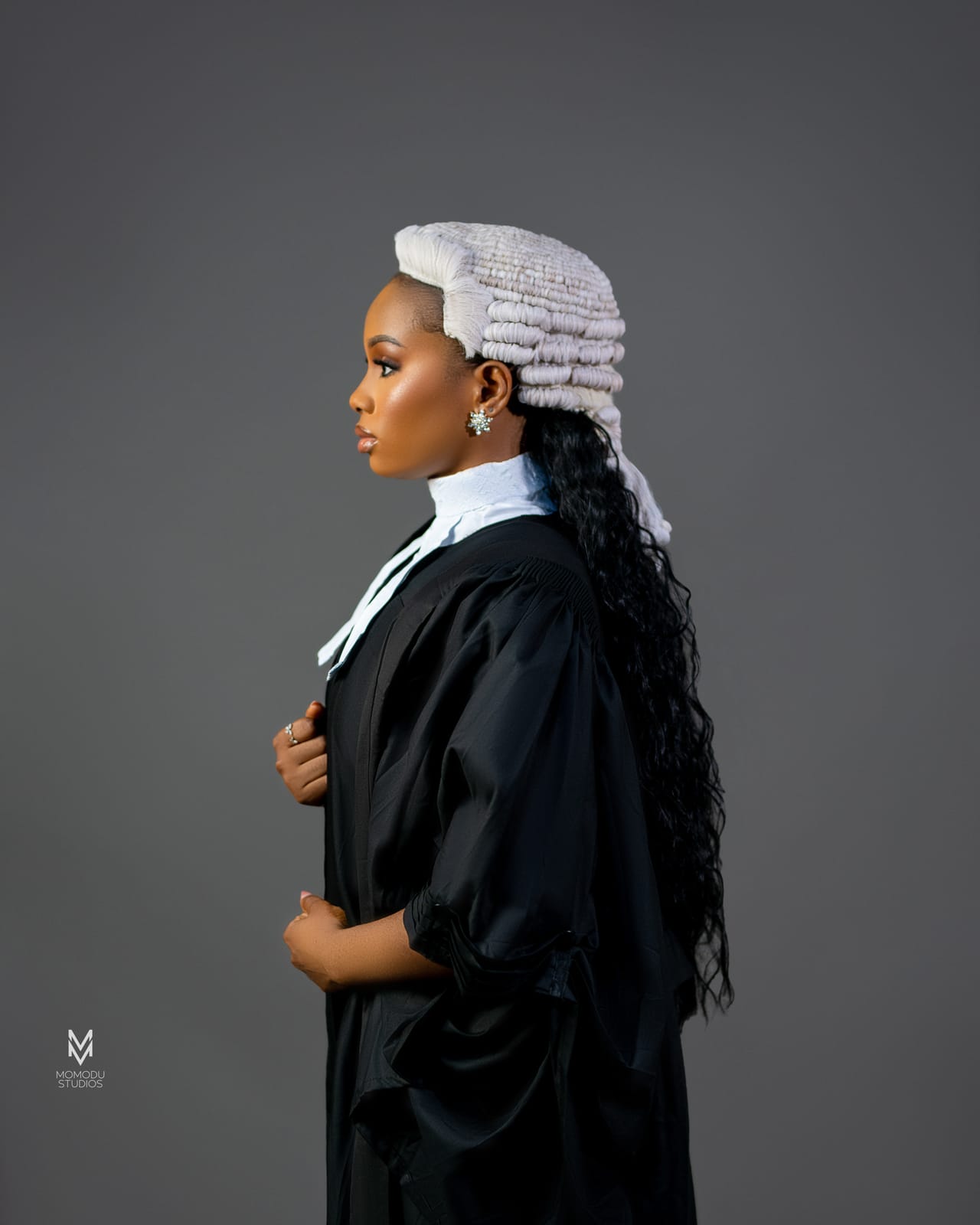 A woman in a barrister's wig and gown photographed in profile against grey