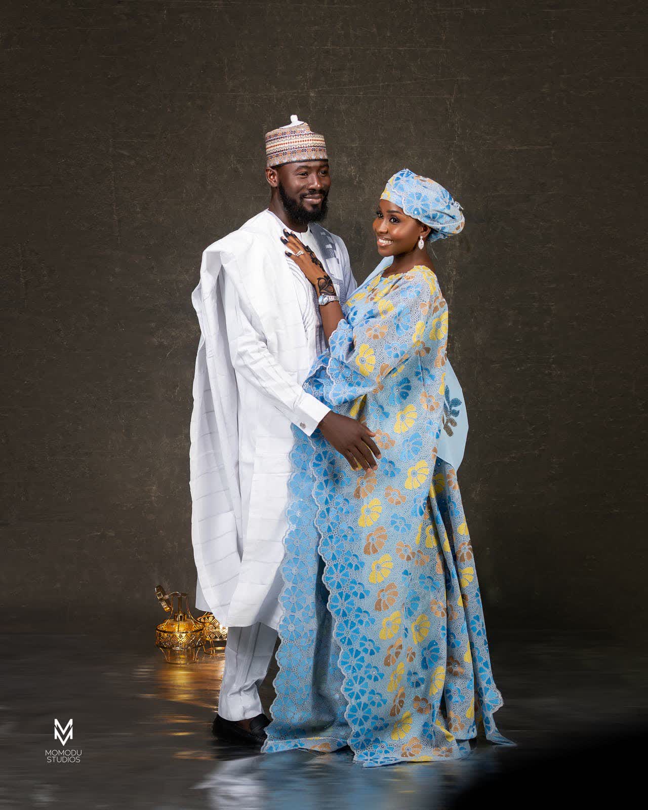 A couple in white agbada and a blue patterned gown with gele, embracing