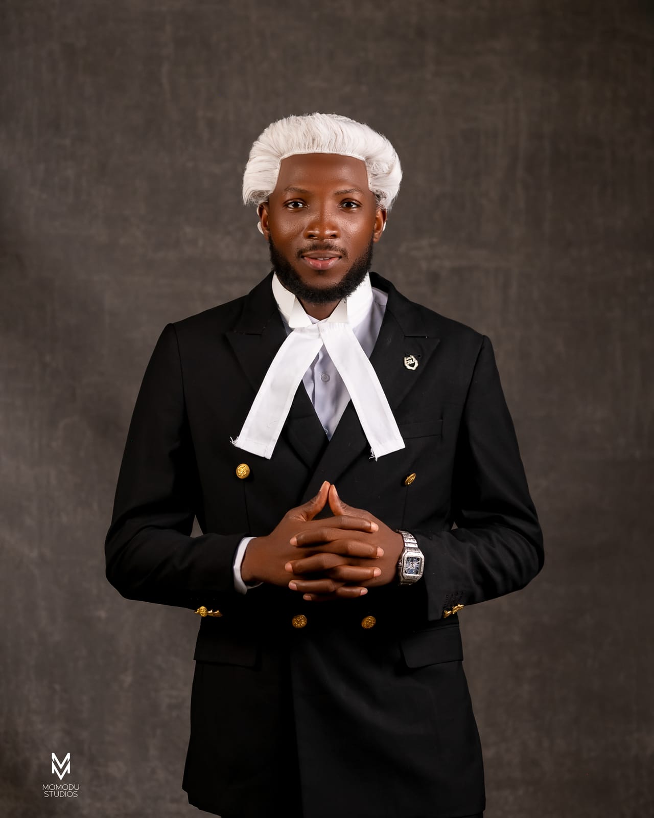 A new lawyer in wig and suit with hands clasped, grey backdrop