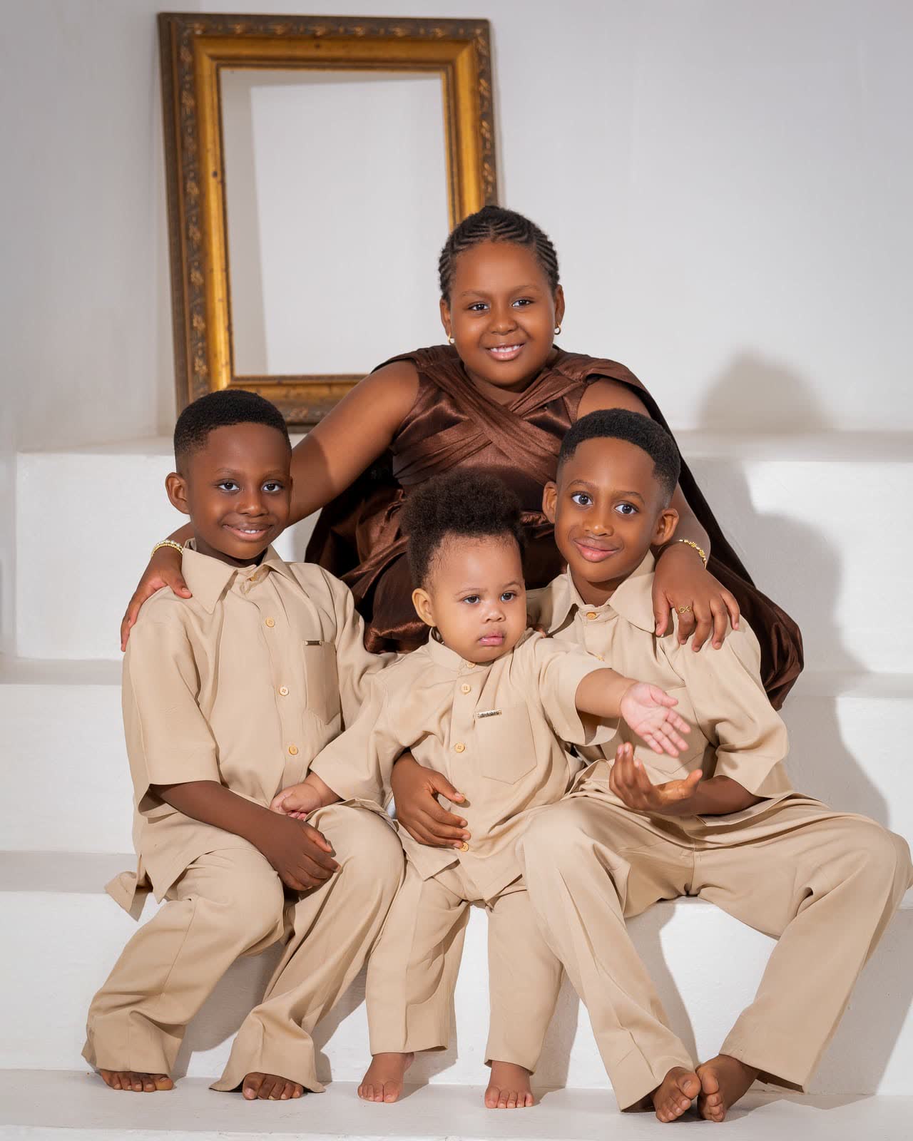 A mother with her three sons in matching beige outfits under an empty gilt frame