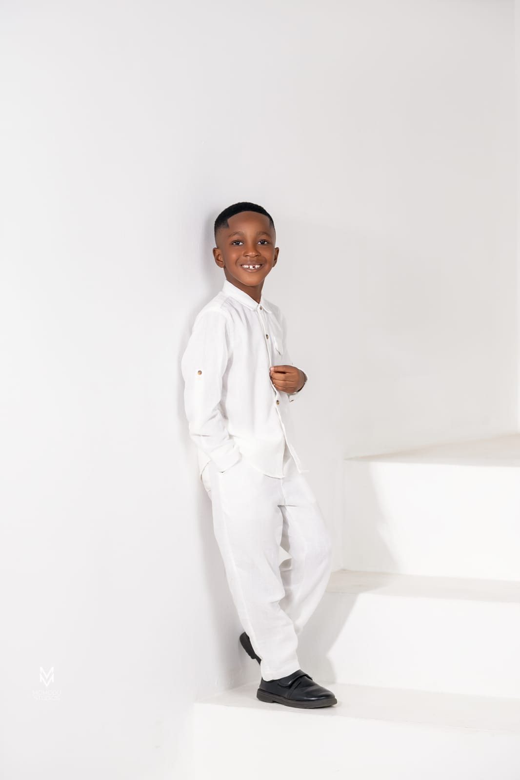 A boy in a white suit standing on white studio steps