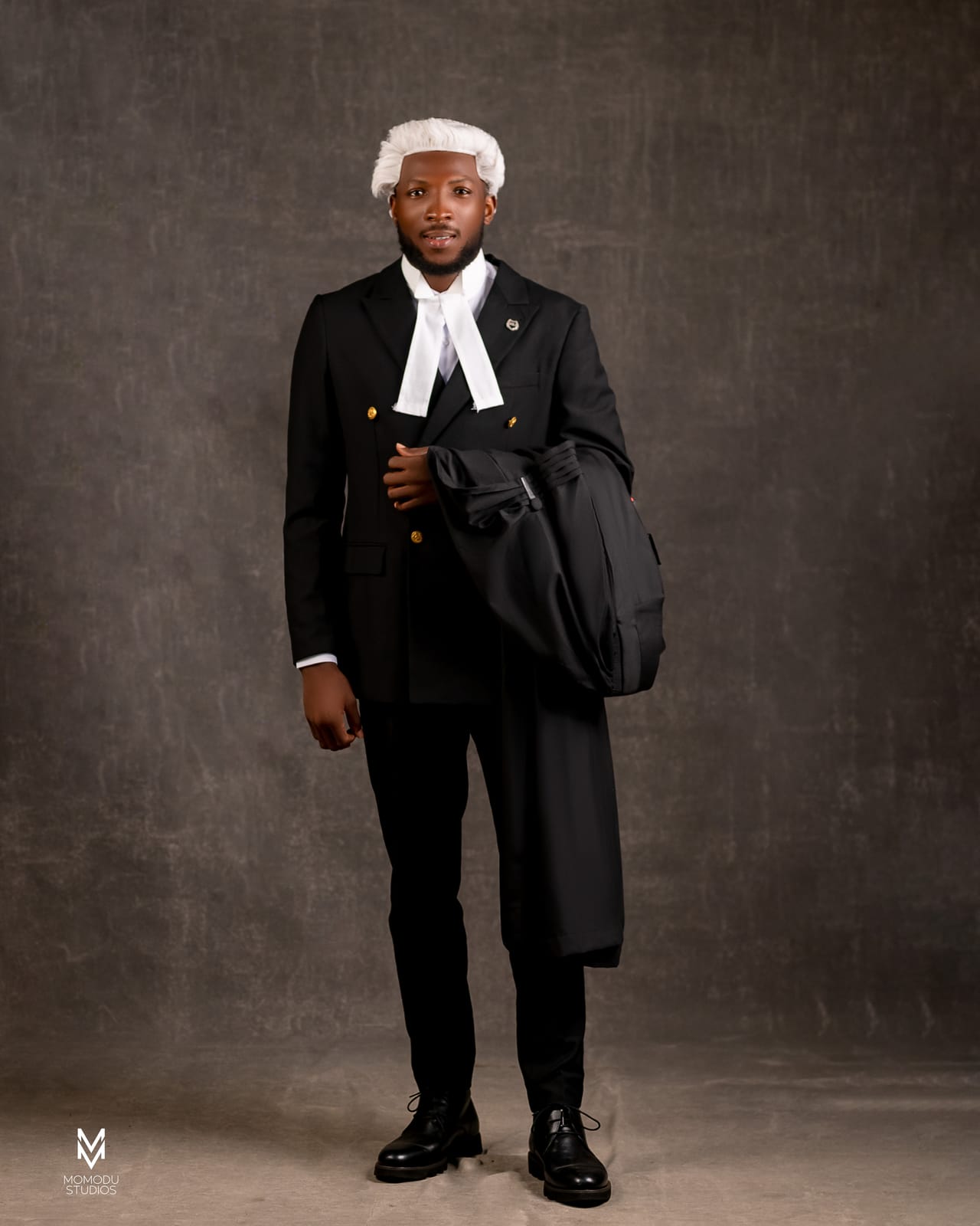 A new lawyer in wig and suit holding his gown over one arm, full length